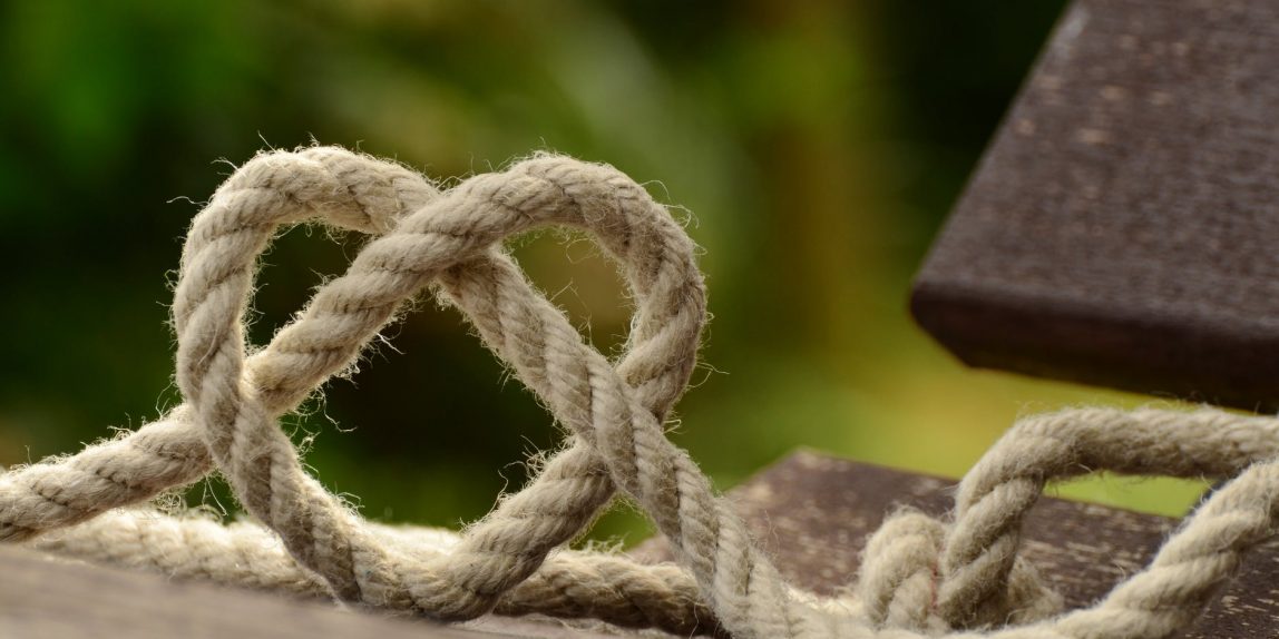 brown rope tangled and formed into heart shape on brown wooden rail